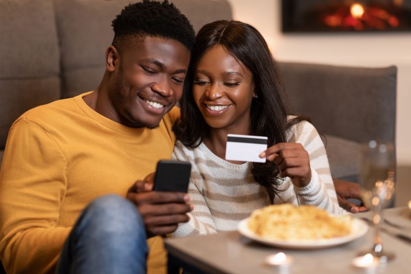 Black Couple Shopping Online On Smartphone Holding Credit Card Indoor